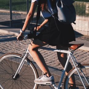 LOCAL Boise apartments resident riding a white bicycle on a sunny day, wearing a black skirt, sneakers, and a backpack.
