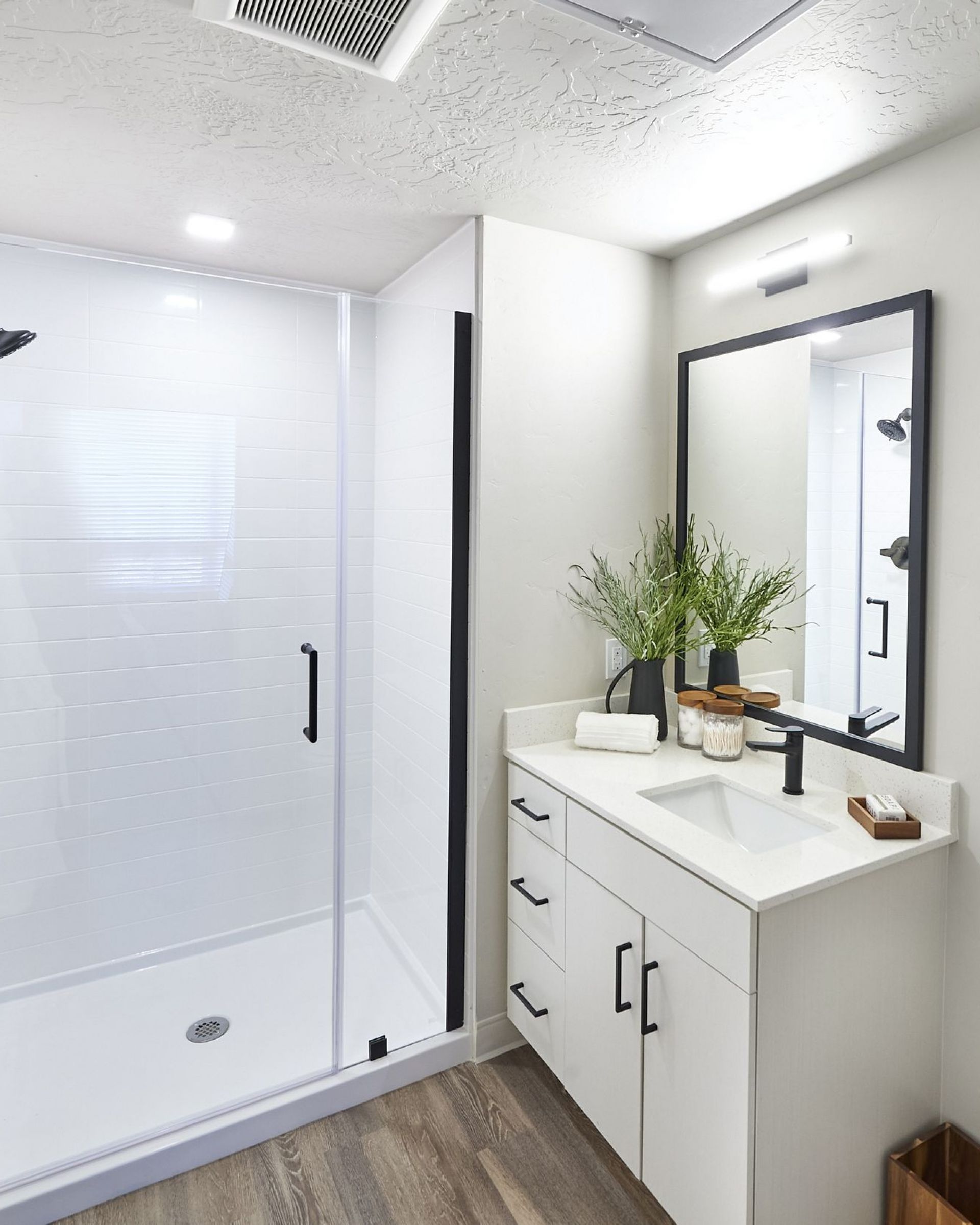 LOCAL Boise modern bathroom with a shower, white vanity, large mirror, plant decor, and wood flooring.