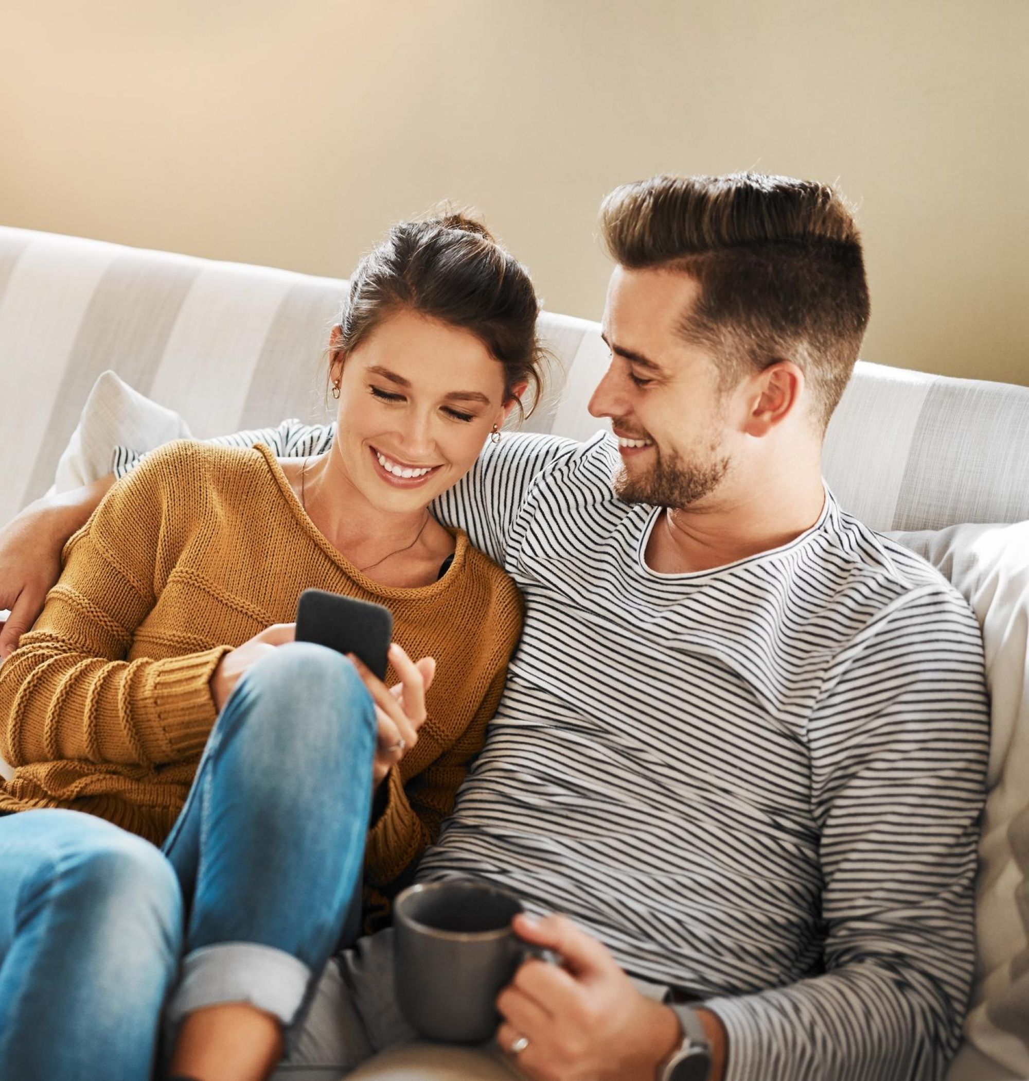 A couple sitting on a couch, smiling while looking at a phone at LOCAL Boise apartments.