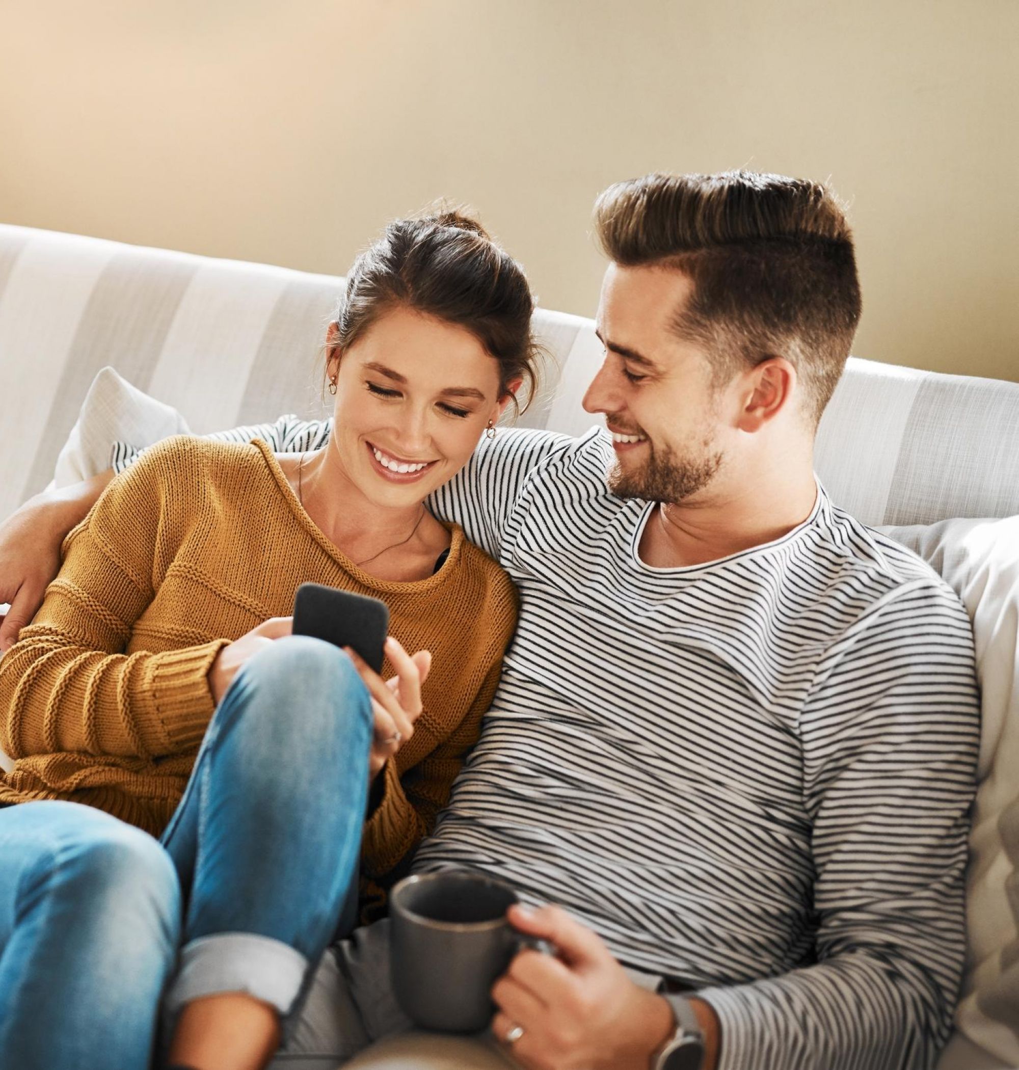 A couple sitting on a couch, smiling while looking at a phone at LOCAL Boise apartments.