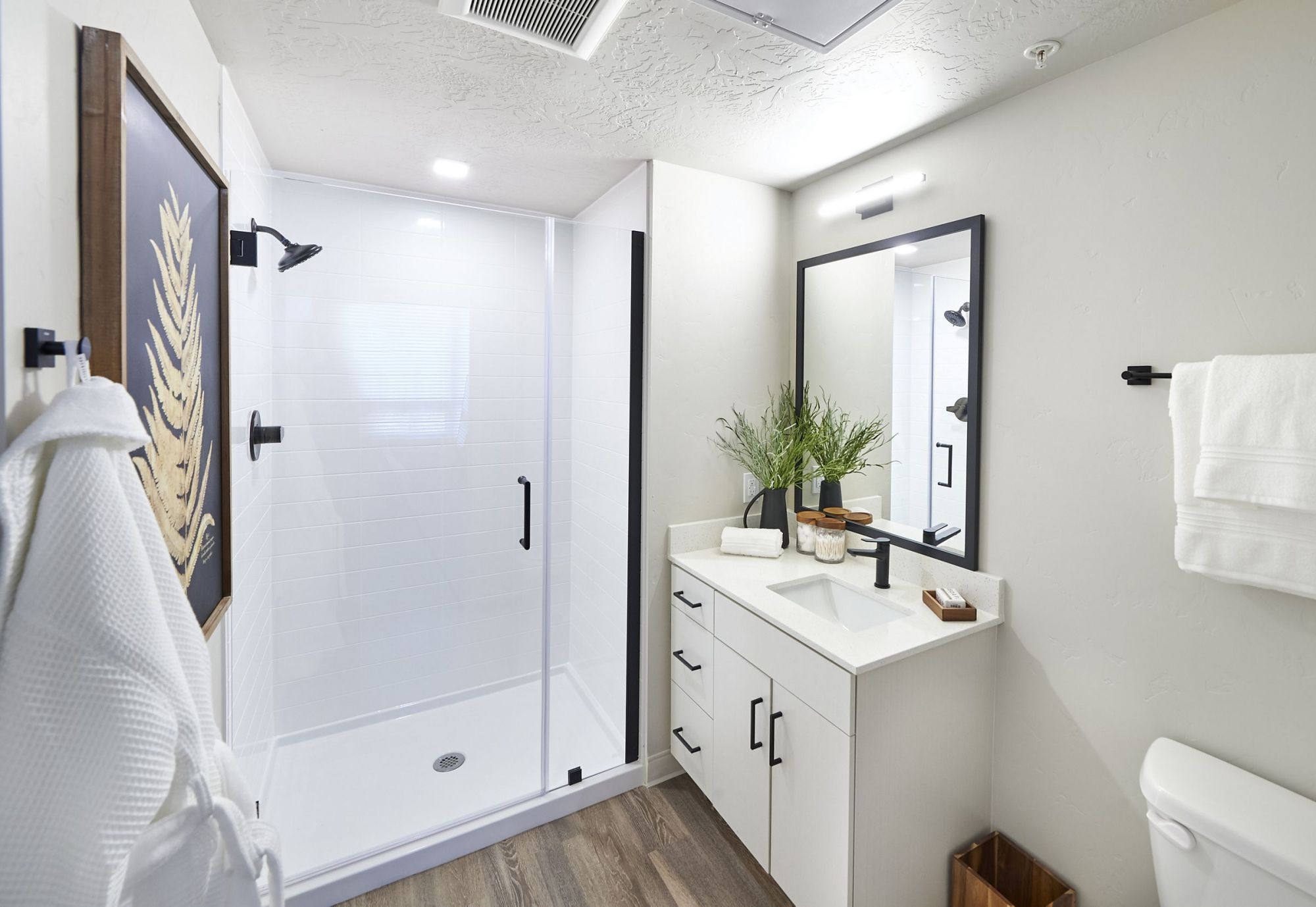 LOCAL Boise modern bathroom with a shower, white vanity, large mirror, plant decor, and wood flooring.