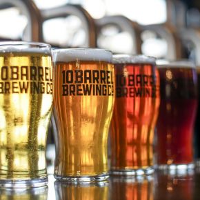 Five glasses of different colored beer from 10 Barrel Brewing Co. lined up on a reflective surface near LOCAL Boise apartments.