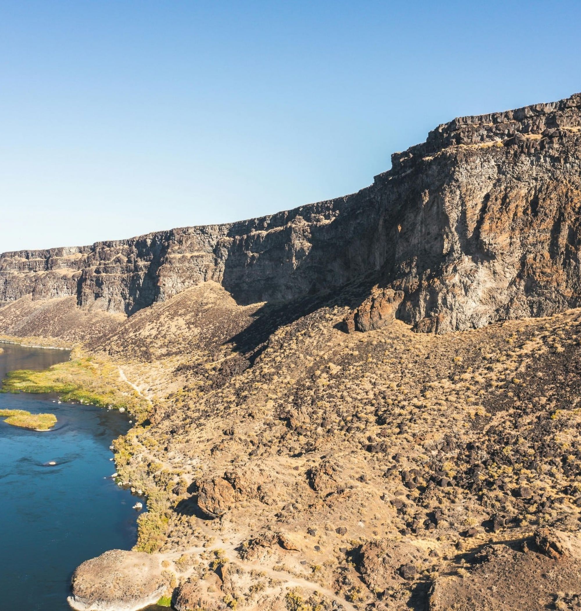 Rocky canyon with steep cliffs beside a winding blue river under a clear blue sky near LOCAL Boise Apartments.