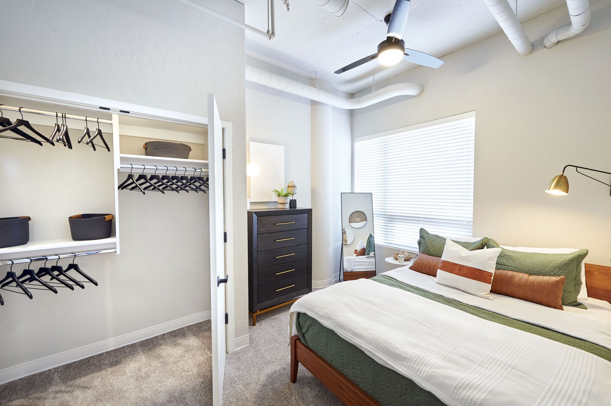 LOCAL Boise modern bedroom with open closet, dresser, bed with green and white bedding, and ceiling fan.